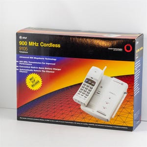 May include: A white AT&T 900 MHz Cordless 9105 telephone set with a base and handset. The box features text including "900 MHz Cordless" and "Belt Clip Included" against a gradient background of orange, yellow, and black.