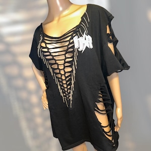 Może przedstawiać: Czarny, oversize'owy T-shirt z dużym wycięciem z przodu i rozcięciami po bokach. Wycięcie jest ozdobione srebrnymi kryształkami, a na koszulce znajduje się biały napis "HSR" z błyskawicą.