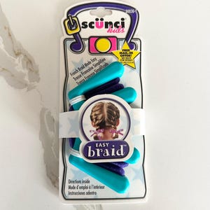 May include: A package of Scunci Kids Easy Braid hair styling tools. The package includes teal and purple hair accessories. The packaging has the words "Easy Braid" and "French Braid Made Easy".