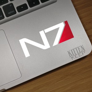 May include: A white N7 logo with a red triangle on a silver laptop. The text "KITTEN KEEP" is below the logo.