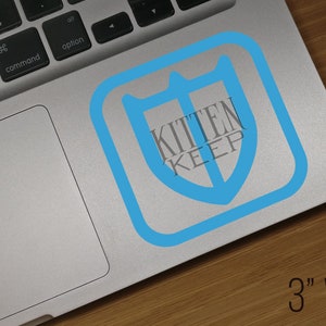 May include: A blue and gray sticker with the text "Kitten Keep" inside a shield shape. The sticker is 3 inches wide and is placed on a silver laptop.