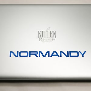 May include: A silver laptop with a blue sticker that says "NORMANDY" and a gray sticker that says "KITTEN KEEP".