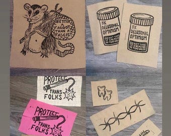 May include: Collection of burlap patches with various black ink illustrations and text. Designs include a badger with text, a bottle of pills, a tooth, barbed wire, a mace, and the phrase "Don't Talk to Cops."