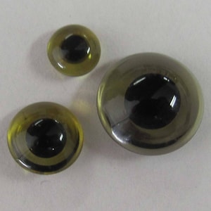 Puede incluir: Tres ojos saltones de plástico de diferentes tamaños. El ojo más grande es plateado con una pupila negra. Los dos ojos más pequeños son amarillos con pupilas negras.