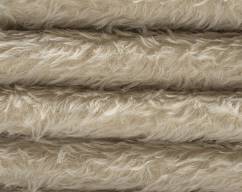 May include: Close-up of a soft, beige faux fur fabric. The fabric is folded in layers, showing the texture and pile of the material.