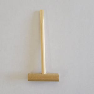 May include: A wooden mallet with a long, thin handle and a rectangular head. The mallet is made of light brown wood.