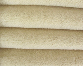 May include: Close-up of a soft, cream-colored fabric with a fuzzy texture. The fabric is folded in layers, creating a smooth, even surface.
