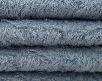 May include: Close-up of a stack of four light blue fuzzy fabric swatches. The fabric has a soft, plush texture.