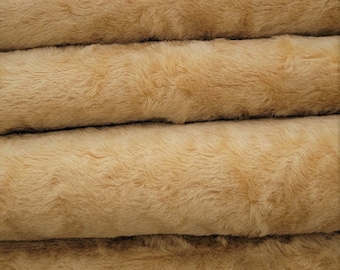 May include: Close-up of a stack of four beige faux fur fabric rolls. The fabric has a soft, fluffy texture.