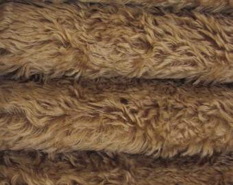 May include: Close-up of a brown faux fur fabric with a soft, fluffy texture. The fabric is folded in layers, showing the depth and texture of the material.