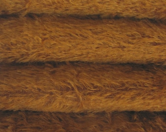 May include: Close-up of a brown fuzzy fabric with a soft, plush texture. The fabric is folded in layers, revealing the depth of the pile.