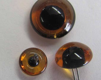 May include: Three amber glass safety eyes with black pupils. The largest eye is 1 inch in diameter and the smallest eye is 1/2 inch in diameter. The smallest eye has a metal post for attaching to a project.