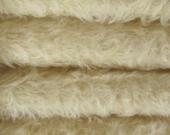 May include: Close-up of a soft, fluffy, cream-colored fabric. The fabric is folded in layers, showing the texture and softness.