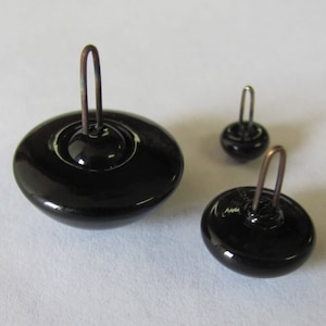May include: Three black glass eyes with metal loops for attaching to a craft project. The eyes are different sizes.