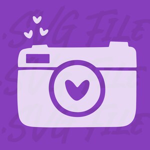 Puede incluir: Una silueta de cámara blanca con un corazón en el objetivo. La cámara está sobre un fondo morado con el texto "SVG FILE" en blanco.