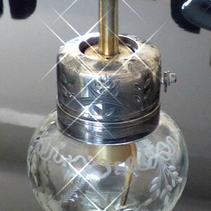 May include: A silver and glass bottle stopper with an etched floral design. The stopper has a round, clear glass base and a silver top with a decorative floral pattern.