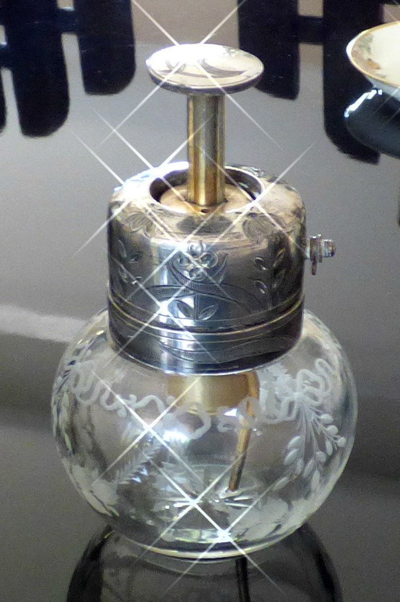 May include: A silver and glass bottle stopper with an etched floral design. The stopper has a round, clear glass base and a silver top with a decorative floral pattern.