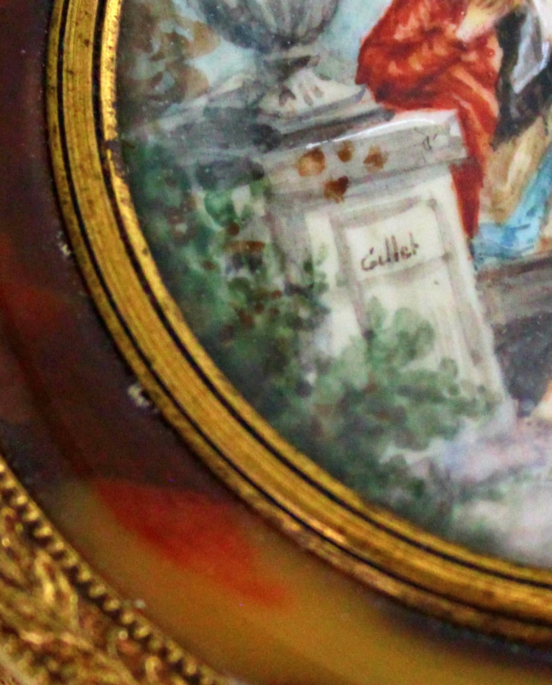 Pu&ograve; includere: Un primo piano di un dipinto in miniatura incorniciato in oro. Il dipinto raffigura una scena con figure in un ambiente da giardino. La firma "Gillet" &egrave; visibile su una struttura in pietra nel dipinto.