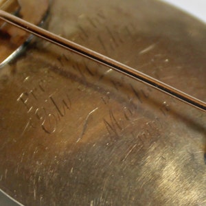 May include: Close-up of the back of a gold-toned brooch with a pin. The brooch is engraved with the text "Pres. Edw. S. Martin, 1901".