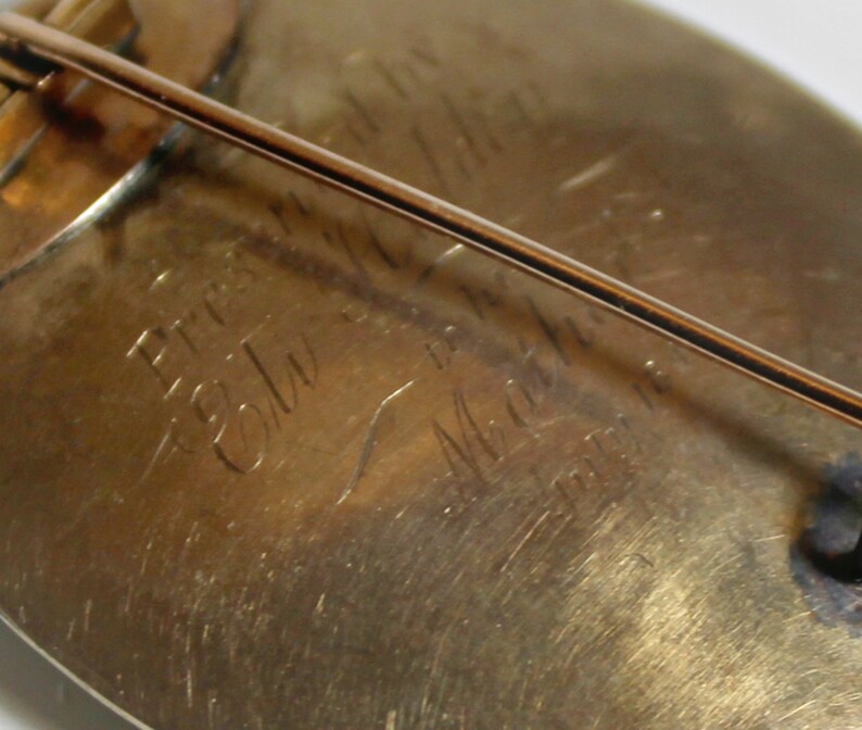 May include: Close-up of the back of a gold-toned brooch with a pin. The brooch is engraved with the text "Pres. Edw. S. Martin, 1901".