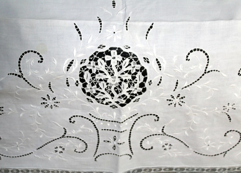 May include: White cotton fabric with intricate white embroidery in a floral pattern. The embroidery features a central circular design with delicate cutouts.