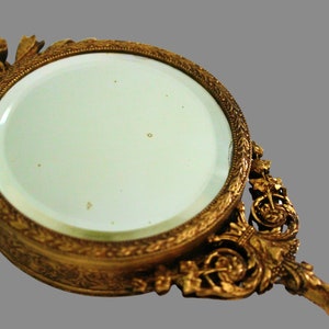 Pu&ograve; includere: Uno specchio da mano dorato con una cornice e un manico decorati. Lo specchio ha una forma circolare e una superficie in vetro trasparente.