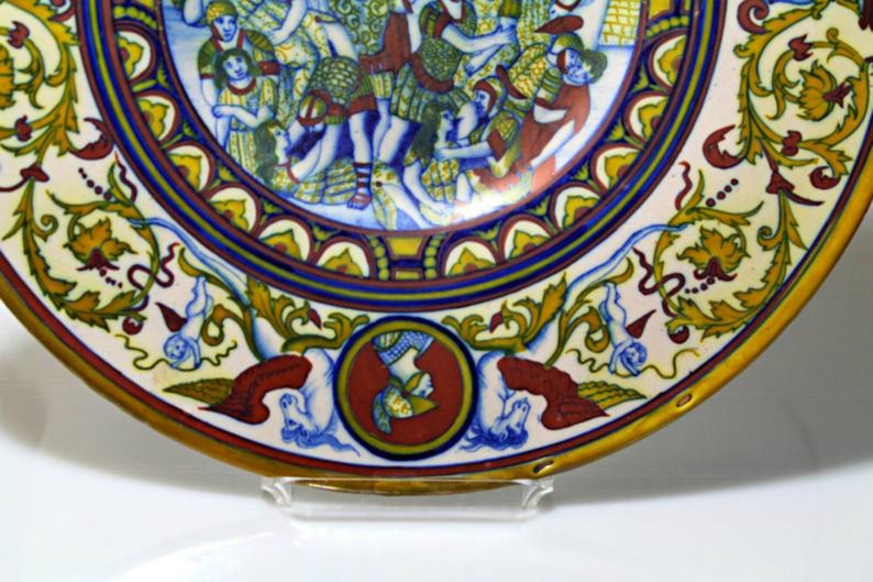 May include: A large, round ceramic plate with a colorful design. The center of the plate features a scene of people dancing, while the outer rim is decorated with intricate floral patterns in shades of blue, yellow, and red.