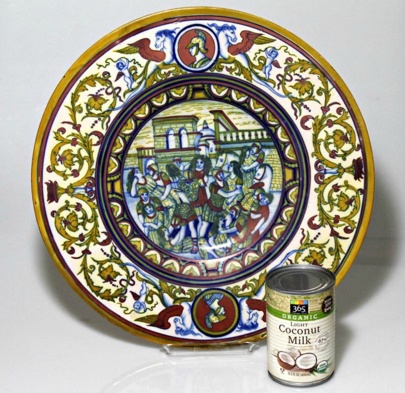 May include: A large, round, ceramic plate with a colorful, intricate design. The plate features a central scene of people in a city setting, surrounded by floral motifs. The plate has a yellow, red, blue, and green color scheme.
