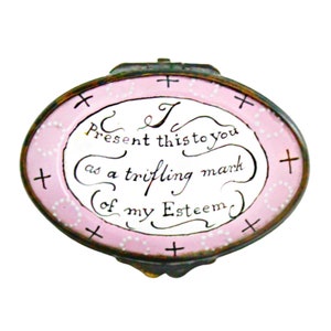 May include: A pink oval-shaped trinket box with a hinged lid. The lid is decorated with white dots and a handwritten message that reads: "I Present this to you as a trifling mark of my Esteem".