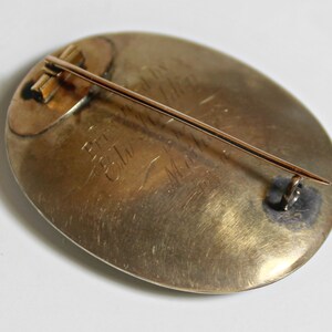 May include: A gold oval brooch with a pin on the back. The brooch has an inscription that reads "Presented to Mrs. C.W. Mead by the Ladies of the First Presbyterian Church".