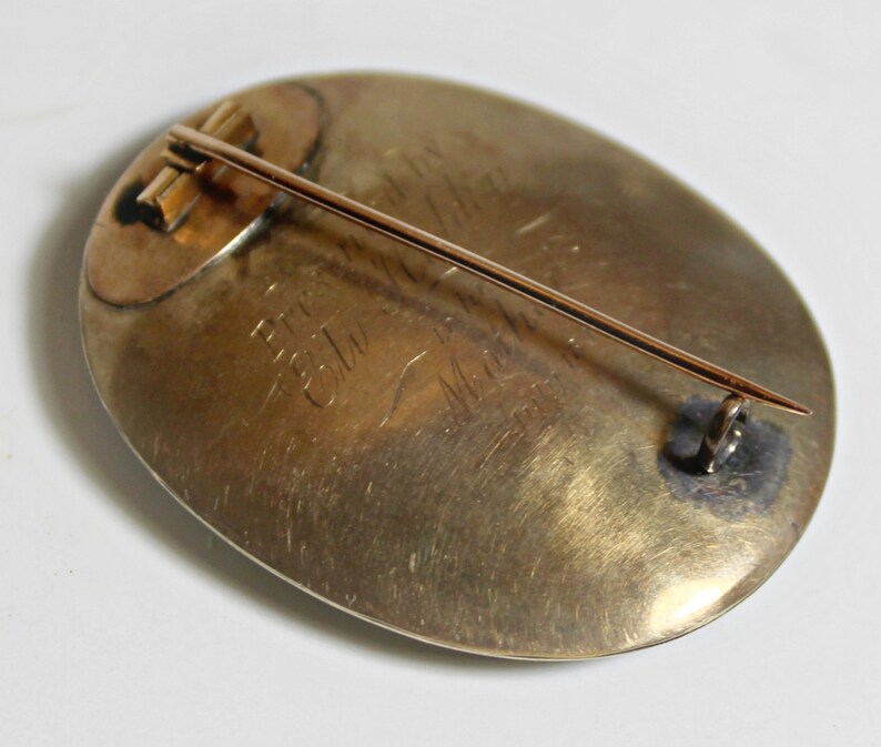 May include: A gold oval brooch with a pin on the back. The brooch has an inscription that reads "Presented to Mrs. C.W. Mead by the Ladies of the First Presbyterian Church".
