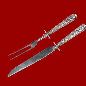 May include: A silver carving set with a knife and fork. Both pieces feature ornate floral designs on the handles.