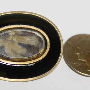 May include: A gold-toned oval locket with a black enamel border. The locket has a glass window that reveals a lock of hair inside.