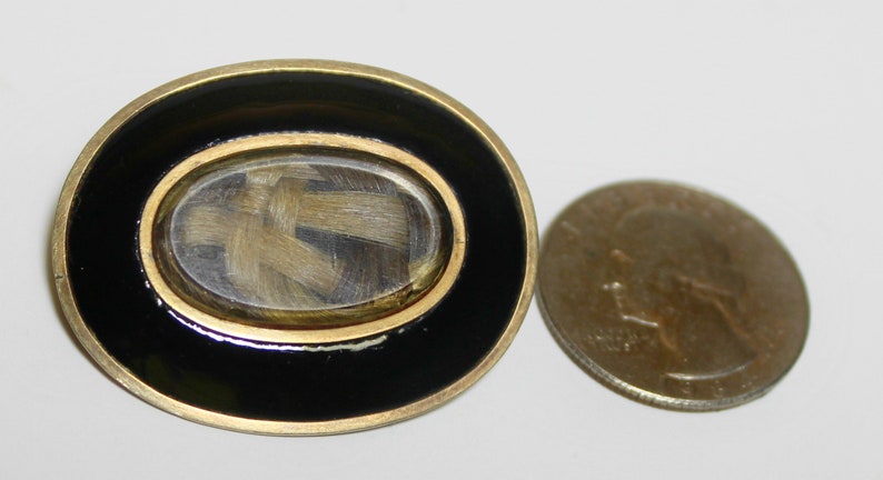 May include: A gold-toned oval locket with a black enamel border. The locket has a glass window that reveals a lock of hair inside.