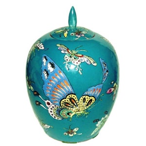 Pode incluir: Um jarro de cerâmica turquesa com uma tampa decorada com borboletas coloridas. O jarro tem um acabamento brilhante e é pintado à mão com detalhes intrincados.