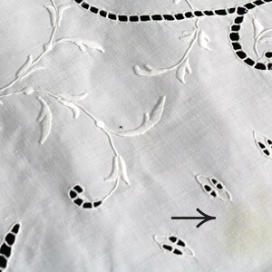 May include: White embroidered tablecloth with a delicate floral pattern. A small yellow stain is visible on the fabric.