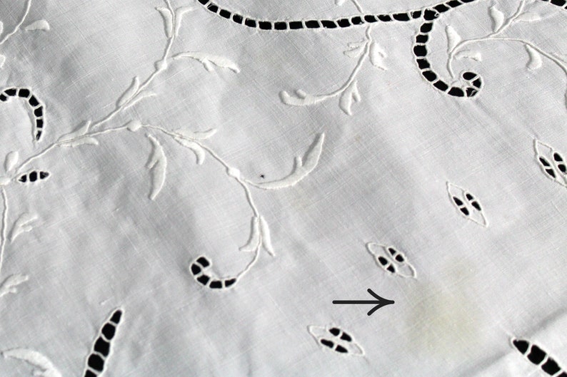 May include: White embroidered tablecloth with a delicate floral pattern. A small yellow stain is visible on the fabric.