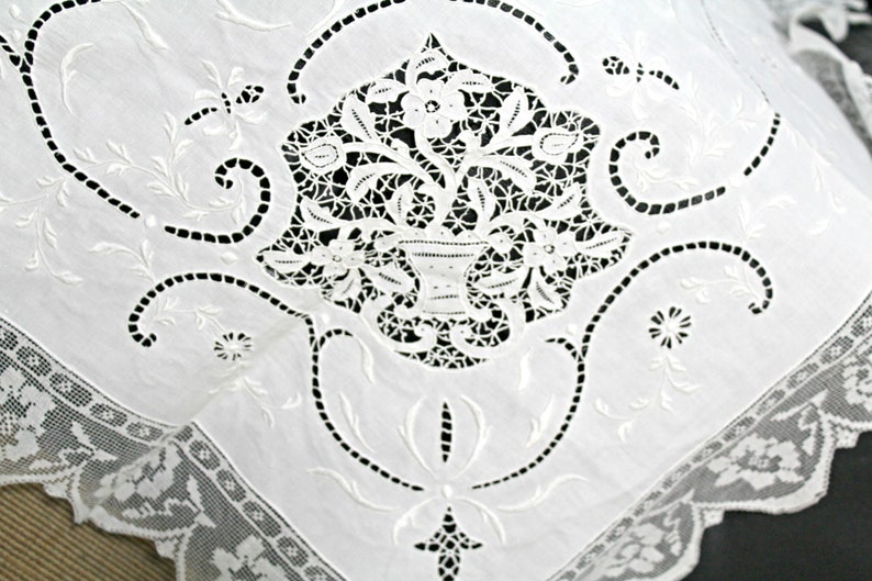 May include: White cotton fabric with intricate embroidered floral designs. The embroidery features delicate flowers and leaves, creating a classic and elegant pattern.