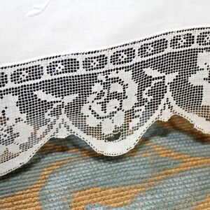 May include: White lace trim with a scalloped edge and a floral pattern. The lace is delicate and intricate, with a fine mesh design.