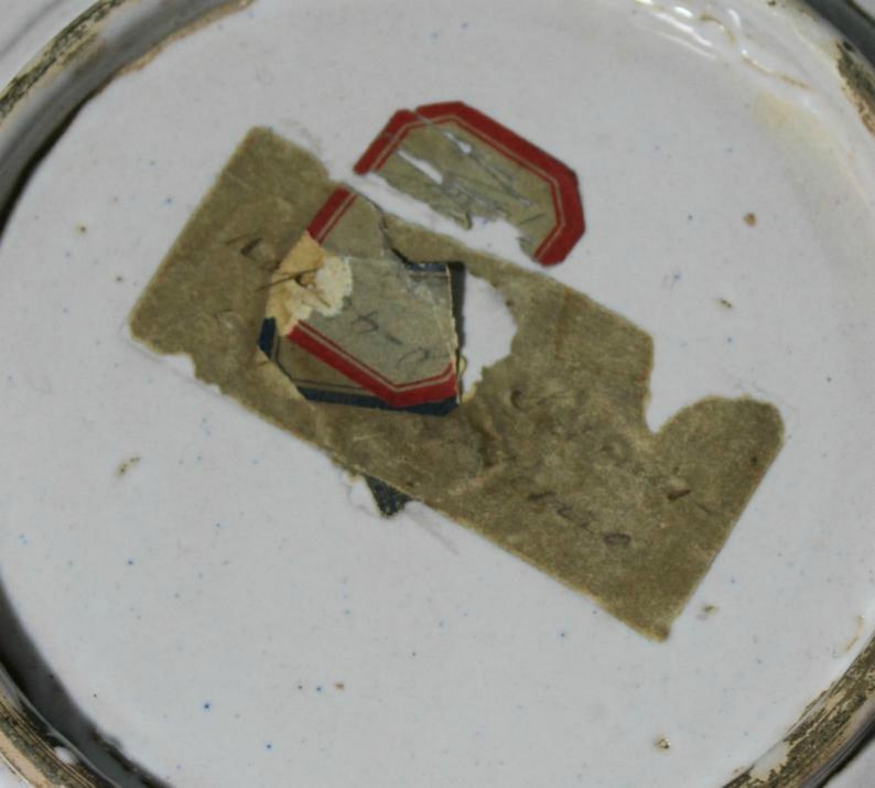 May include: Close-up of a white ceramic plate with a brown paper label that says "14-1-14" and a red and blue label with a faded image.
