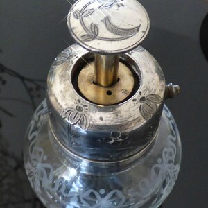 May include: Silver and glass bottle stopper with a floral design and a crescent moon on the top. The stopper has a brass base and a silver top.