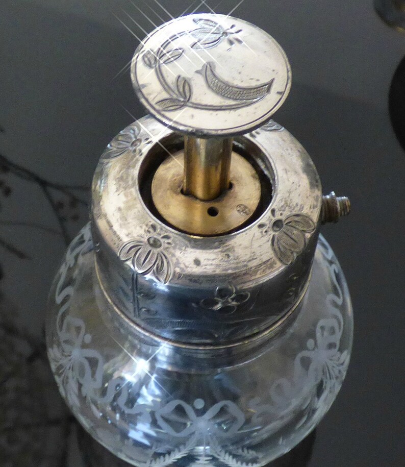 May include: Silver and glass bottle stopper with a floral design and a crescent moon on the top. The stopper has a brass base and a silver top.