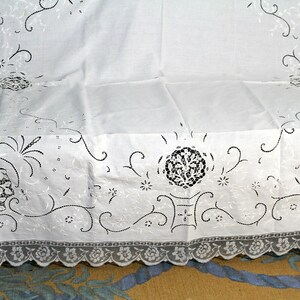 May include: White tablecloth with a delicate lace border and intricate embroidered floral designs in black thread.