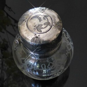 May include: A clear glass inkwell with a silver lid. The lid is decorated with an etched floral design. The inkwell is also decorated with an etched floral design.