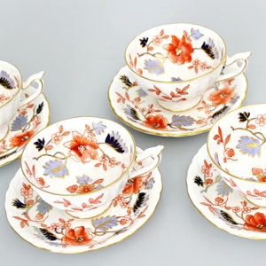 May include: Set of four white teacups and saucers with a floral pattern in shades of orange, blue, and gold. The floral pattern features delicate leaves and flowers.