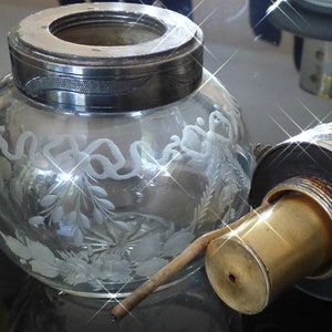 May include: A clear glass bottle with a silver top and a brass spout. The bottle is decorated with etched floral designs.