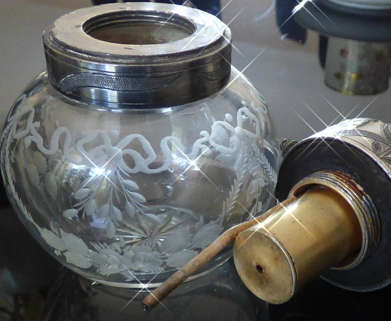 May include: A clear glass bottle with a silver top and a brass spout. The bottle is decorated with etched floral designs.