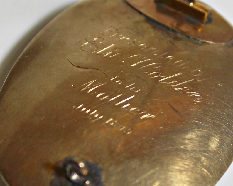 May include: A gold-toned oval brooch with an inscription that reads "Presented to Mrs. Golden for her many years of service".