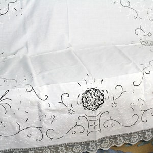 May include: White cotton tablecloth with delicate embroidered floral designs in black thread. The tablecloth has a scalloped edge with a lace trim.