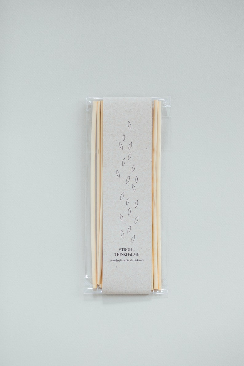 May include: A package of natural, light-colored drinking straws. The straws are bundled together and wrapped in clear plastic. A light brown paper label with leaf-like illustrations and text is visible.
